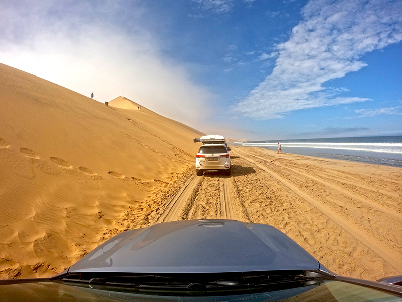 4x4 vehicles driving along the narrow beach corridor between dunes and surf at low tide