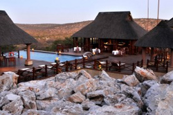 Scenic view of the luxurious swimming pool area at Epacha Game Lodge, surrounded by traditional thatched roofs, Aus, Namibia