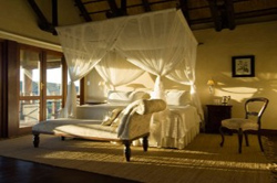 Luxurious royal chalet room at Epacha Game Lodge, Aus, Namibia, featuring a king-size bed, mosquito nets, and a cozy chaise lounge by the glass doors overlooking the Epacha Private Game Reserve.